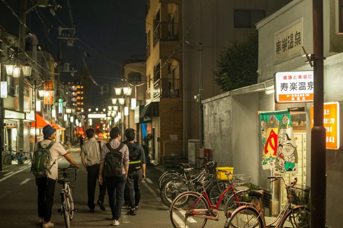 A neighbourhood bathhouse in Osaka at night, with a lit sign, a banner at the door and bicycles parked outside